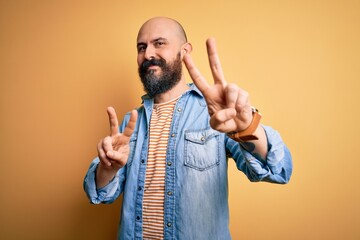 Wall Mural - Handsome bald man with beard wearing casual denim jacket and striped t-shirt smiling looking to the camera showing fingers doing victory sign. Number two.