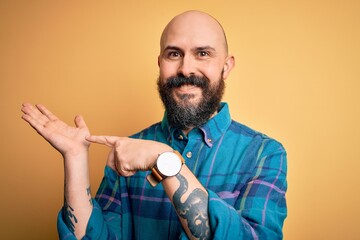 Poster - Handsome bald man with beard wearing casual shirt standing over isolated yellow background amazed and smiling to the camera while presenting with hand and pointing with finger.