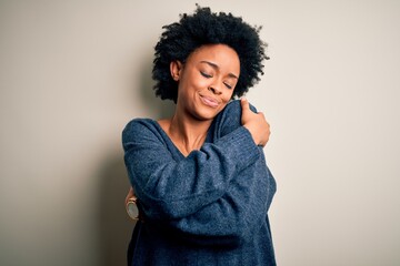 Young beautiful African American afro woman with curly hair wearing casual sweater Hugging oneself happy and positive, smiling confident. Self love and self care