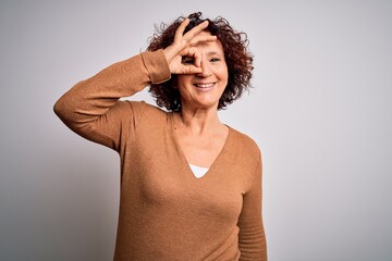 Poster - Middle age beautiful curly hair woman wearing casual sweater over isolated white background doing ok gesture with hand smiling, eye looking through fingers with happy face.