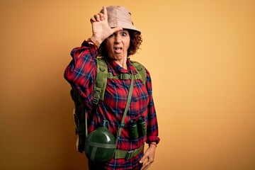 Poster - Middle age curly hair hiker woman hiking wearing backpack and water canteen using binoculars making fun of people with fingers on forehead doing loser gesture mocking and insulting.