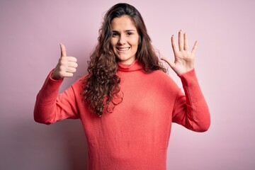 Young beautiful woman with curly hair wearing turtleneck sweater over pink background showing and pointing up with fingers number six while smiling confident and happy.