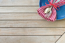 A Red White And Blue Picnic Table Place Setting With Napkin, Fork And Spoon And Plate In An Upper Corner On Horizontal Wood Board Table Top Background With Room Or Space For Copy, Text Or Your Words.