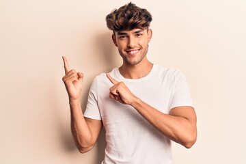 Young hispanic man wearing casual clothes smiling and looking at the camera pointing with two hands and fingers to the side.