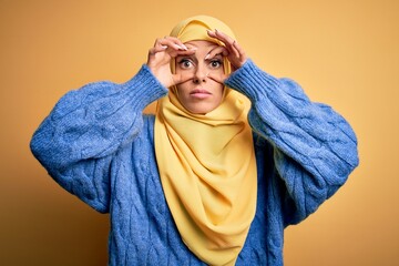 Wall Mural - Young beautiful brunette muslim woman wearing arab hijab over isolated yellow background Trying to open eyes with fingers, sleepy and tired for morning fatigue