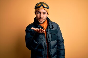 Canvas Print - Young handsome skier man with beard wearing snow sportswear and ski goggles looking at the camera blowing a kiss with hand on air being lovely and sexy. Love expression.