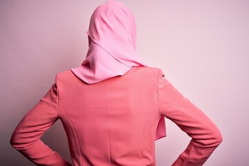 Young beautiful girl wearing muslim hijab standing over isolated pink background standing backwards looking away with arms on body