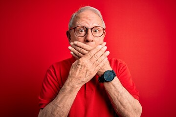 Wall Mural - Grey haired senior man wearing glasses and casual t-shirt over red background shocked covering mouth with hands for mistake. Secret concept.