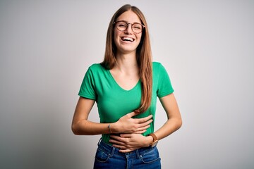 Wall Mural - Young beautiful redhead woman wearing casual green t-shirt and glasses over white background smiling and laughing hard out loud because funny crazy joke with hands on body.