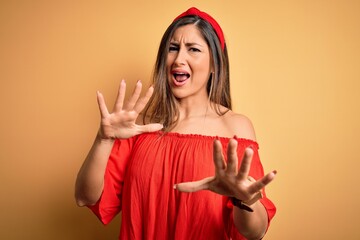 Wall Mural - Young beautiful woman colorful summer style over yellow isolated background afraid and terrified with fear expression stop gesture with hands, shouting in shock. Panic concept.