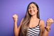 © Krakenimages.com - Young beautiful woman wearing casual summer striped top over purple isolated background very happy and excited doing winner gesture with arms raised, smiling and screaming for success. Celebration