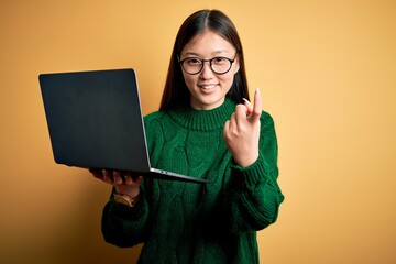 Sticker - Young asian business woman wearing glasses and working using computer laptop Beckoning come here gesture with hand inviting welcoming happy and smiling