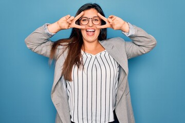 Sticker - Young hispanic business woman wearing glasses standing over blue isolated background Doing peace symbol with fingers over face, smiling cheerful showing victory