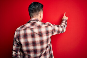 Young handsome caucasian man wearing casual modern shirt over red isolated background Posing backwards pointing ahead with finger hand