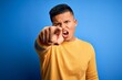© Krakenimages.com - Young handsome latin man wearing yellow casual sweater over isolated blue background pointing displeased and frustrated to the camera, angry and furious with you