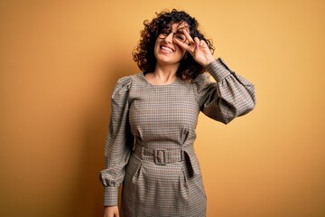 Wall Mural - Beautiful arab business woman wearing dress and glasses standing over yellow background Doing peace symbol with fingers over face, smiling cheerful showing victory