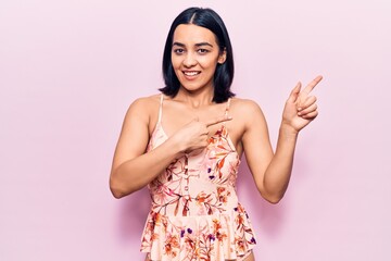 Young beautiful latin woman wearing casual clothes smiling and looking at the camera pointing with two hands and fingers to the side.