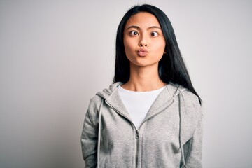 Wall Mural - Young beautiful chinese sporty woman wearing sweatshirt over isolated white background making fish face with lips, crazy and comical gesture. Funny expression.