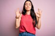 Young brunette woman wearing casual summer shirt over pink isolated background relaxed and smiling with eyes closed doing meditation gesture with fingers. Yoga concept.