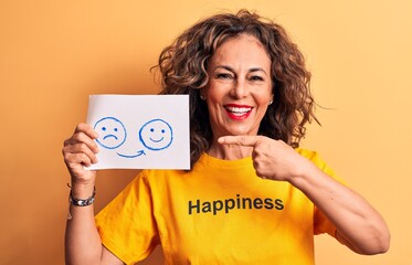 Middle age woman wearing t-shirt with happiness word holding sad to happy emotions paper smiling happy pointing with hand and finger