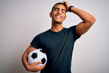 Handsome african american man playing footbal holding soccer ball over white background smiling confident touching hair with hand up gesture, posing attractive and fashionable