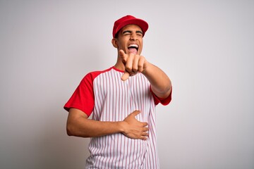 Young handsome african american sportsman wearing striped baseball t-shirt and cap laughing at you, pointing finger to the camera with hand over body, shame expression