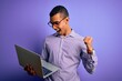 © Krakenimages.com - Young handsome african american business man working using laptop over purple background screaming proud and celebrating victory and success very excited, cheering emotion