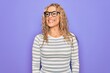 © Krakenimages.com - Beautiful blonde woman wearing casual striped t-shirt and glasses over purple background looking away to side with smile on face, natural expression. Laughing confident.