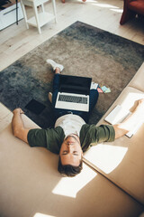 tired caucasian man with bristle lying on floor and sofa after working at the laptop with a book