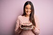 © Krakenimages.com - Young beautiful brunette woman holding birthday delicious cake over pink background with a happy face standing and smiling with a confident smile showing teeth