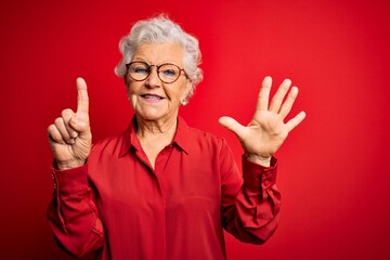 Wall Mural - Senior beautiful grey-haired woman wearing casual shirt and glasses over red background showing and pointing up with fingers number six while smiling confident and happy.