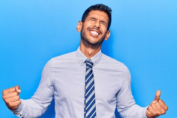 Sticker - Young latin man wearing business clothes very happy and excited doing winner gesture with arms raised, smiling and screaming for success. celebration concept.