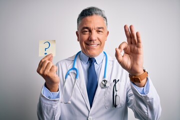 Canvas Print - Middle age handsome grey-haired doctor man holding paper with question mark doing ok sign with fingers, excellent symbol