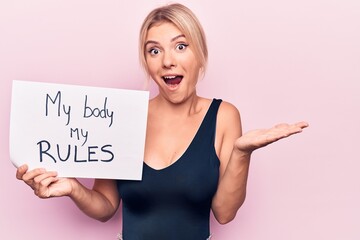 Young blonde woman asking for women freedom holding paper with my body my rules message celebrating achievement with happy smile and winner expression with raised hand