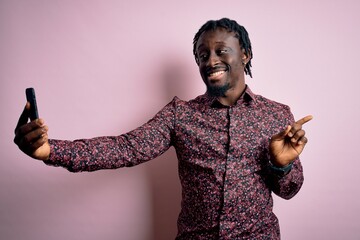 Sticker - Young handsome african american man wearing casual shirt standing making selfie by camera very happy pointing with hand and finger to the side