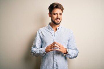 Wall Mural - Young handsome man with beard wearing striped shirt standing over white background Hands together and fingers crossed smiling relaxed and cheerful. Success and optimistic