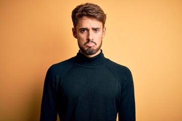 Wall Mural - Young handsome man with beard wearing turtleneck sweater standing over yellow background depressed and worry for distress, crying angry and afraid. Sad expression.