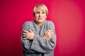 Wall Mural - Young blonde woman with modern short hair wearing casual sweater over pink background shaking and freezing for winter cold with sad and shock expression on face