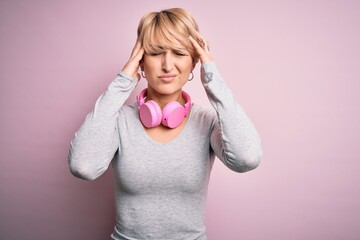 Poster - Young blonde woman with short hair wearing headphones on neck over pink background suffering from headache desperate and stressed because pain and migraine. Hands on head.