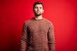 © Krakenimages.com - Young blond man with beard and blue eyes wearing casual sweater over red background with serious expression on face. Simple and natural looking at the camera.