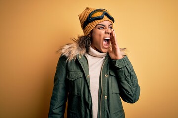 Wall Mural - Young african american afro skier girl wearing snow sportswear and ski goggles shouting and screaming loud to side with hand on mouth. Communication concept.