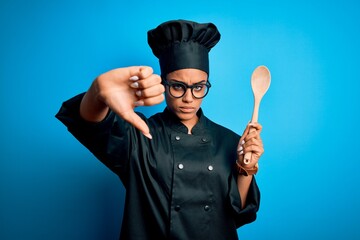 Sticker - Young african american chef girl wearing cooker uniform and hat holding wooden spoon tool with angry face, negative sign showing dislike with thumbs down, rejection concept