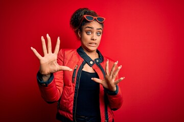 Sticker - Beautiful african american girl wearing red jacket and sunglasses over isolated background afraid and terrified with fear expression stop gesture with hands, shouting in shock. Panic concept.