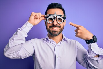 Sticker - Young handsome optical man with beard wearing optometry glasses over purple background very happy pointing with hand and finger