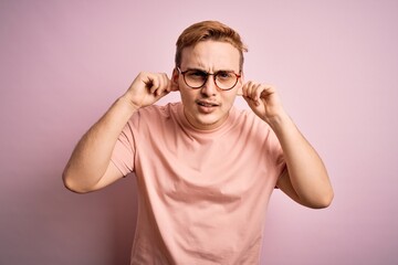 Wall Mural - Young handsome redhead man wearing casual t-shirt standing over isolated pink background Smiling pulling ears with fingers, funny gesture. Audition problem