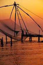 Silhouette Of Fisherman Fishing With Large Net During Sunset In Cochin - India 
