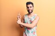 © Krakenimages.com - Young handsome man with beard wearing summer sleeveless t-shirt smiling and looking at the camera pointing with two hands and fingers to the side.
