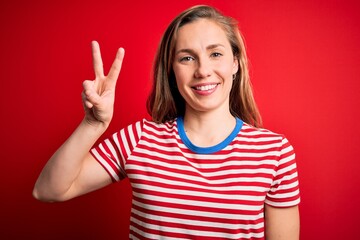 Sticker - Young beautiful blonde woman wearing casual striped t-shirt over isolated red background showing and pointing up with fingers number two while smiling confident and happy.