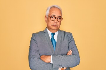 Canvas Print - Middle age senior grey-haired handsome business man wearing glasses over yellow background skeptic and nervous, disapproving expression on face with crossed arms. Negative person.