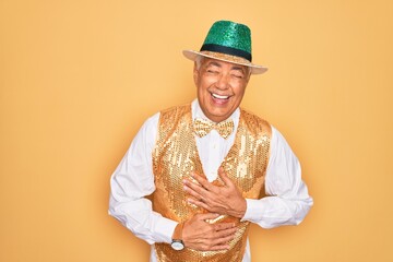 Wall Mural - Middle age senior grey-haired man wearing Brazilian carnival custome over yellow background smiling and laughing hard out loud because funny crazy joke with hands on body.